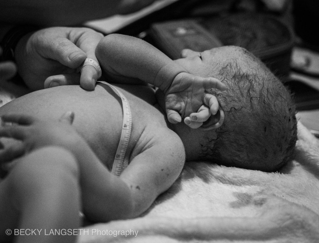 A newly born baby is measured by his midwife during a newborn exam in Seattle, Washington. This image was captured by a birth photographer and show the value of hiring a birth photographer.