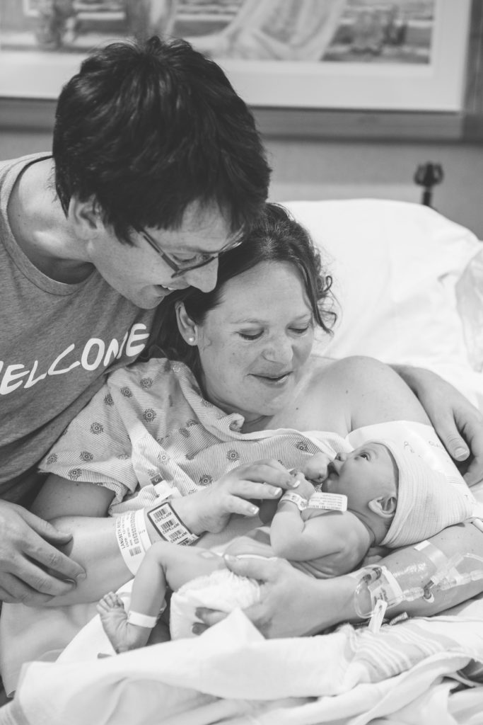 a professional photo taken by a birth photographer of a couple and their new baby in the hospital bed after giving birth.