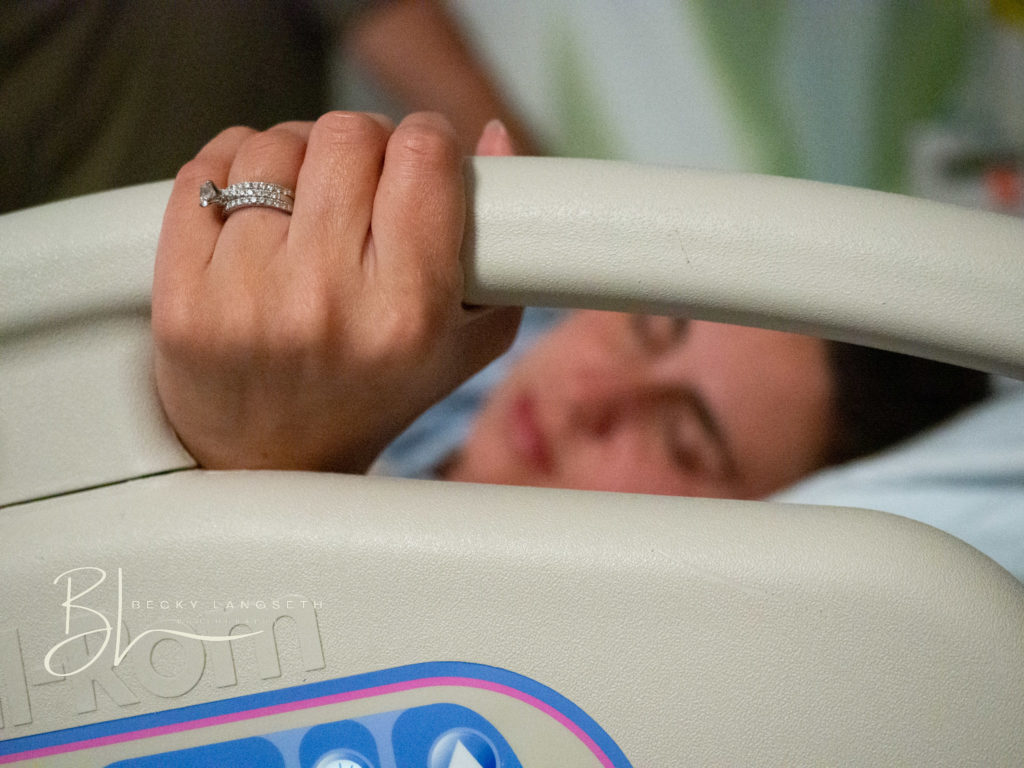 a woman's hand is holding the hospital bed with her ring in focus as she labors at a maternity center at Evergreen Hospital in Kirkland, WA. Image is taken by seattle birth photographer, Becky langseth.