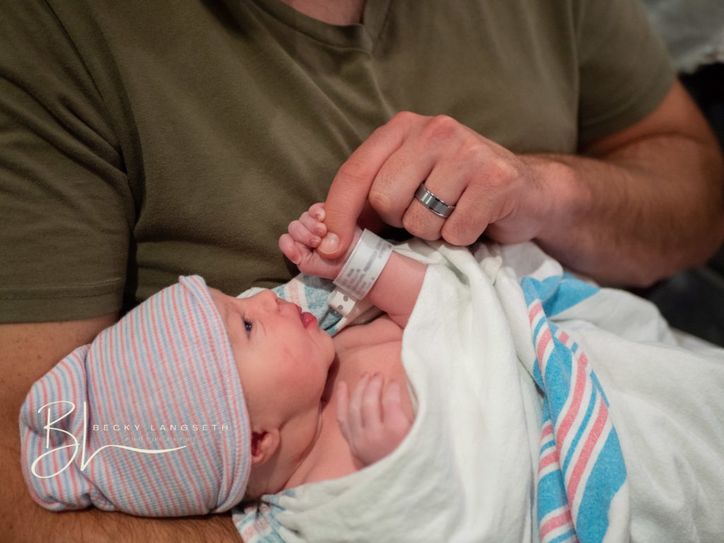 A new dad holds his new baby at at Evergreen Hospital in Kirkland, WA. The dad's finger is being held by the tiny newborns little hand. This image shows the value of birth photography taken by seattle birth photographer, Becky Langseth.