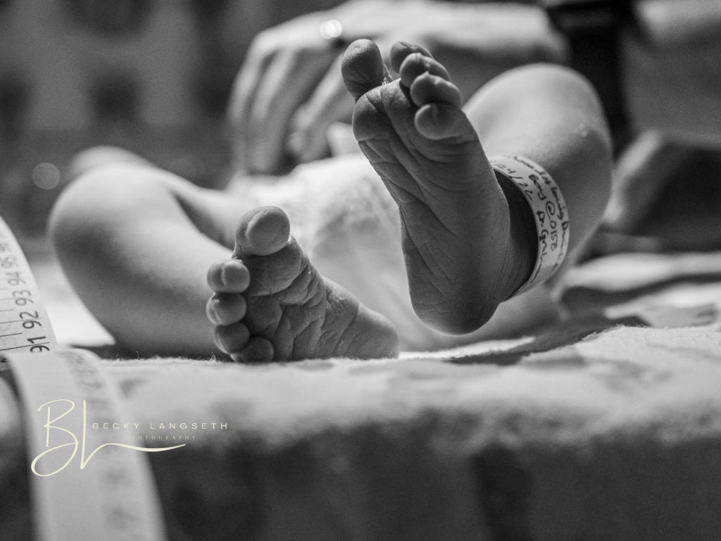 tiny feet of a newborn baby laying in a hospital warming bed at Overlake Childbirth Center in Bellevue, WA is about to be measured for it's newborn exam. This image is an example debunking misconceptions about birth photography and how birth photos are beautiful. 