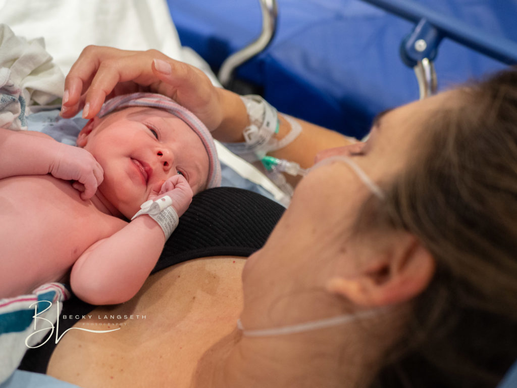 A mother gently touches her newborn's face as she holds her baby on her chest after undergoing a c-section birth, captured by Seattle birth photographer, Becky Langseth.
