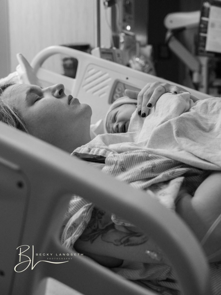 A mother laying in a hospital bed is holding her baby for the first time. She has a calm look on her face with her eyes closed, taking in the moment. This is an amazing example of overcoming honest misconceptions about birth photography and shows how birth photography is beautiful and worth the investment. 