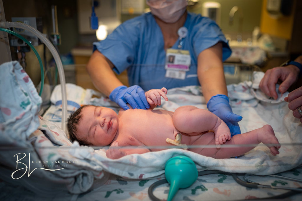 a newborn is being examined in the warming bed moments after being born at UW Medical Center at Montlake in Seattle, WA. This image was taken after a full day of labor, and is a great example of why birth photography can be so expensive!