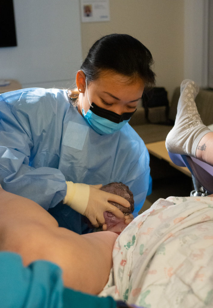 An OBGYN is helping a newborn baby to be delivered. The OBGYN is holding the baby's head as it comes out.