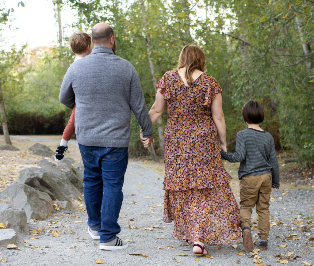 A family is walking along the gravel path a Wallace Swamp Creek Park in Kenmore, WA holding hands.
