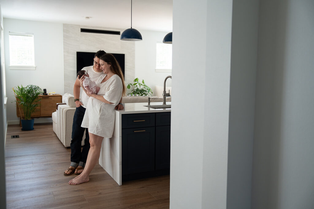 boy giggles a couple stand in their kitchen holding and admiring their baby