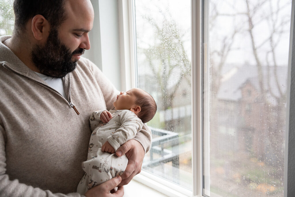 Edmonds Family Photographer a new dad holding her brand newborn baby at home on a Seattle rainy day