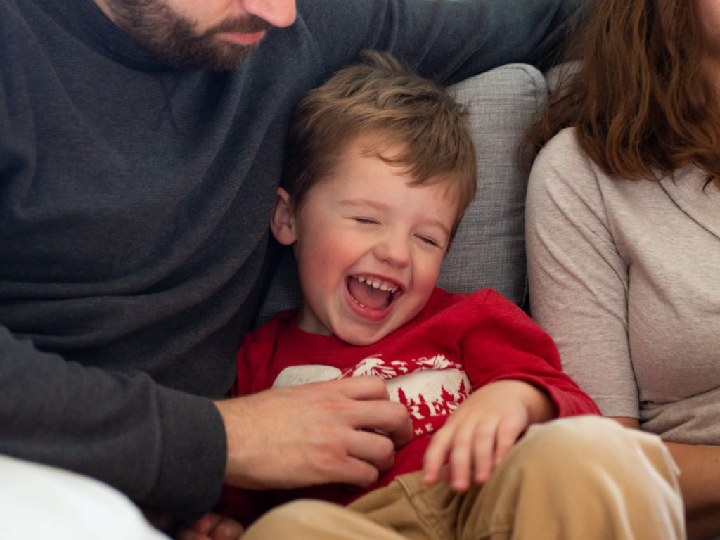 a little boy giggles as his father hold him during an in home photoshoot.
