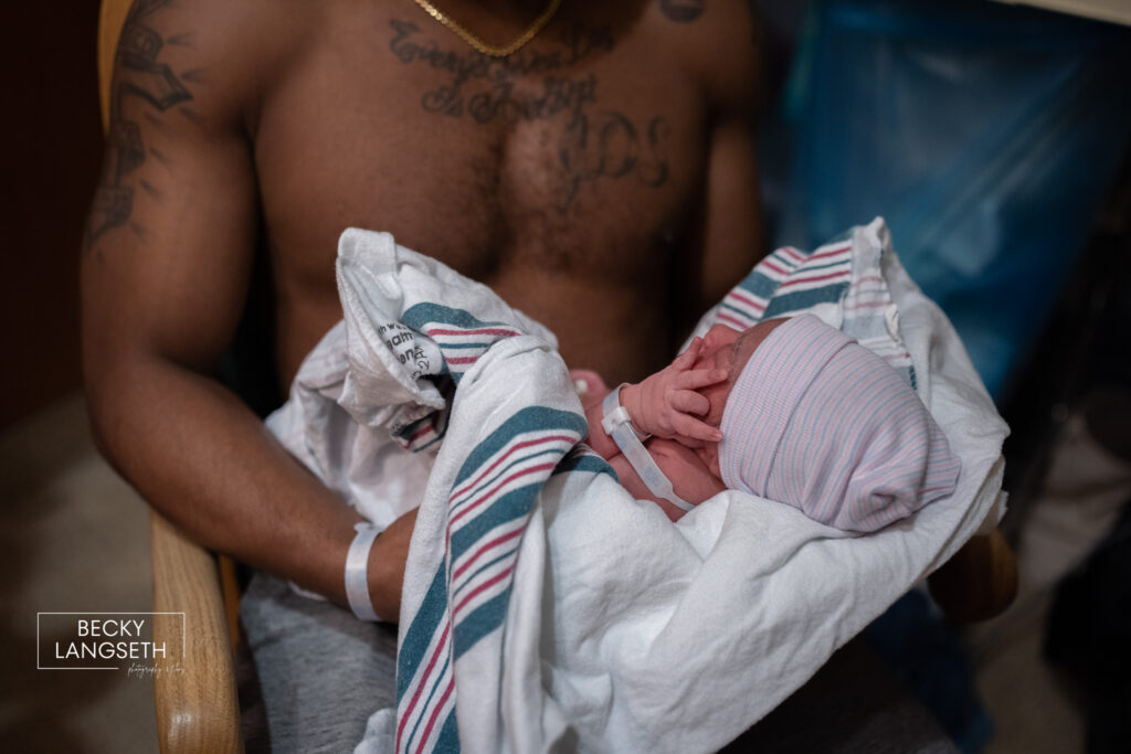image of a new dad without a shirt on, holding his baby girl for the first time about to do some skin-to-skin with his new baby.