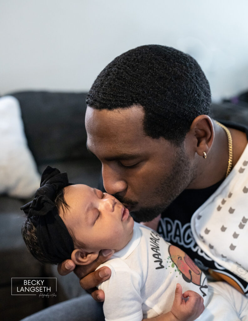 A father kisses his newborn baby at home during an in home newborn photography session in Washington state.