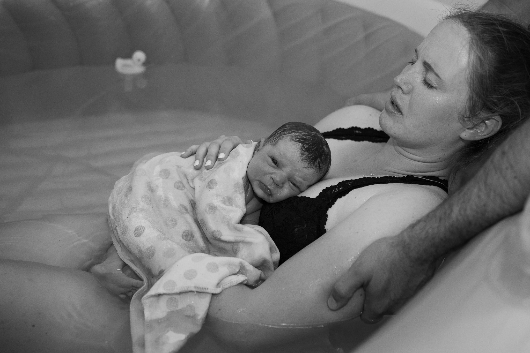 A mother holds her new baby while still sitting in the birthing pool at a home birth in Seattle.