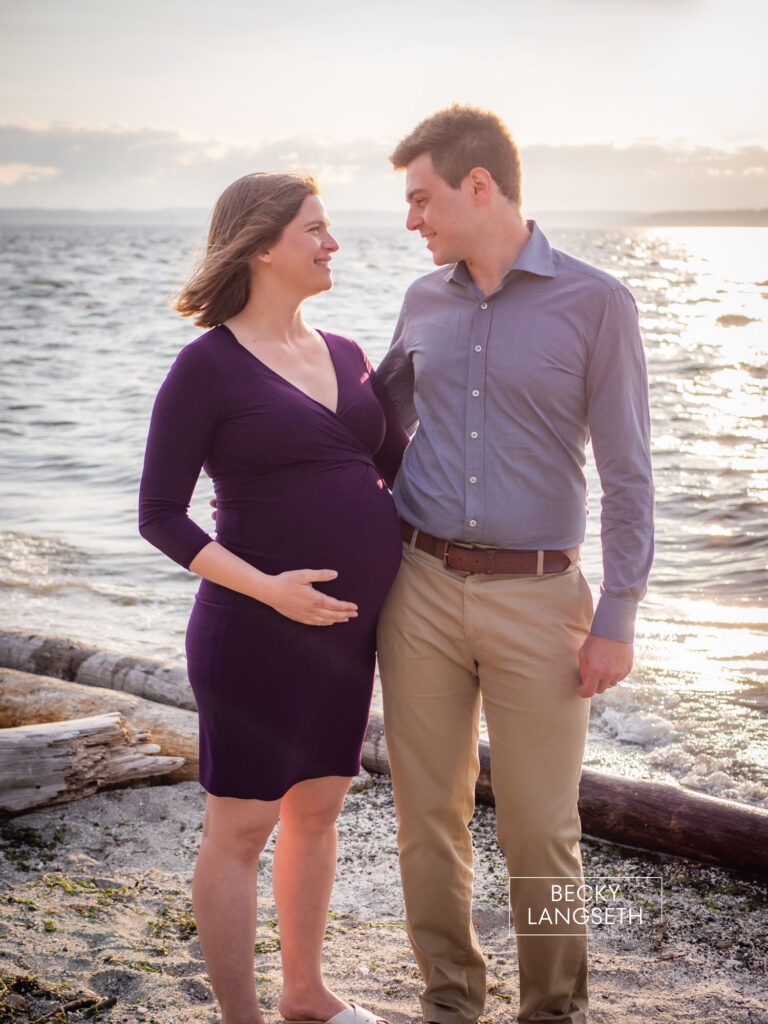 A pregnant couple look at each other at Carkeek Park excited about their new baby arriving soon as they get their professional photos taken which is an example of how to enjoy your third trimester of pregnancy.