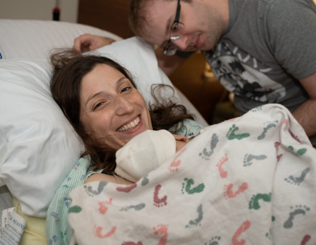 Answering common questions about birth photography by showing this photo of a mother smiling with joy as she holds her baby recently born at Swedish Issaquah Hospital.