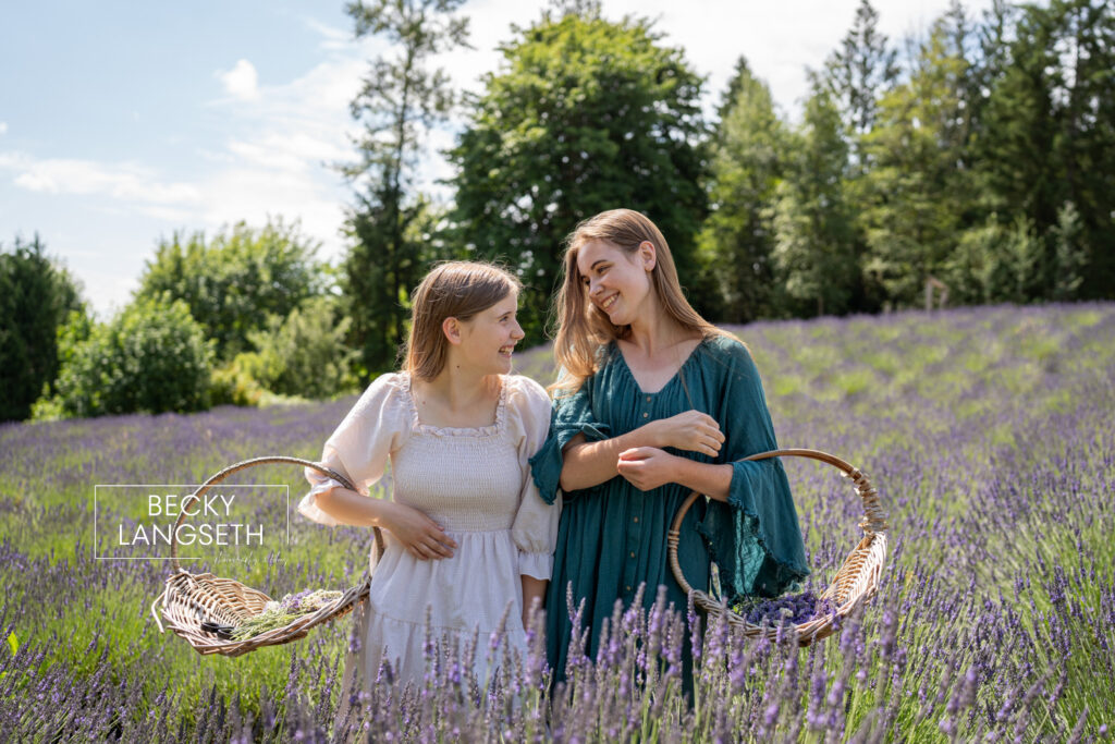 two girls holding baskets giggling at each other while standing in a lavender field at Purple Robe Lavender Farm