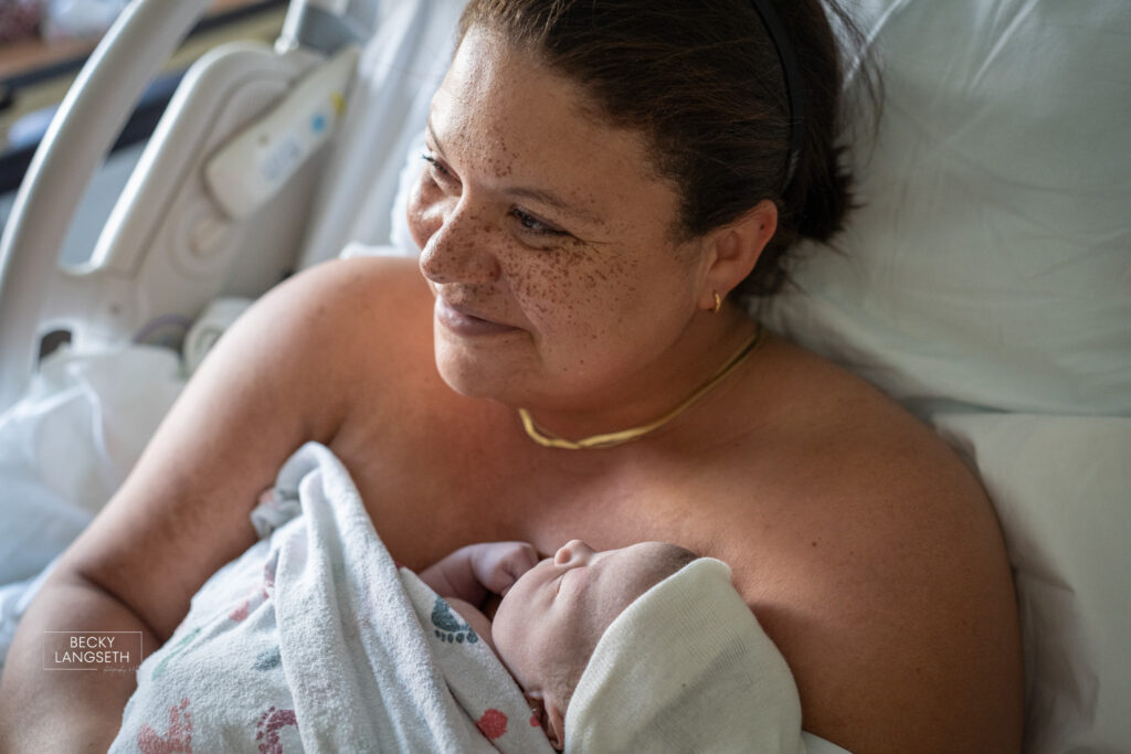 A mother smiles as she holds her brand new infant skin-to-skin.