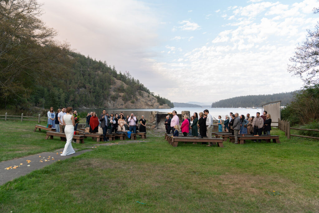 Bride walks down the aisle with the view of Cornet Bay in the background at her Deception Pass wedding.