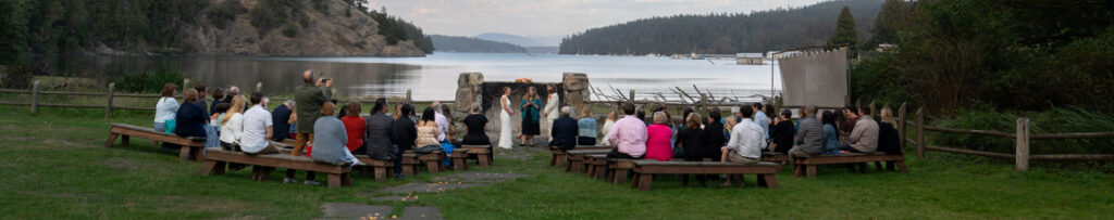 A wide angle view of a wedding ceremony in progress with Cornet Bay in the background