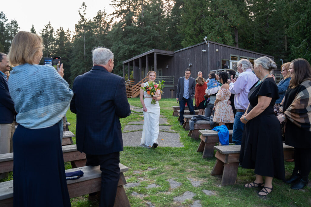 Bride smiles as she walks down the aisle for her wedding at Cornet Bay Retreat Center