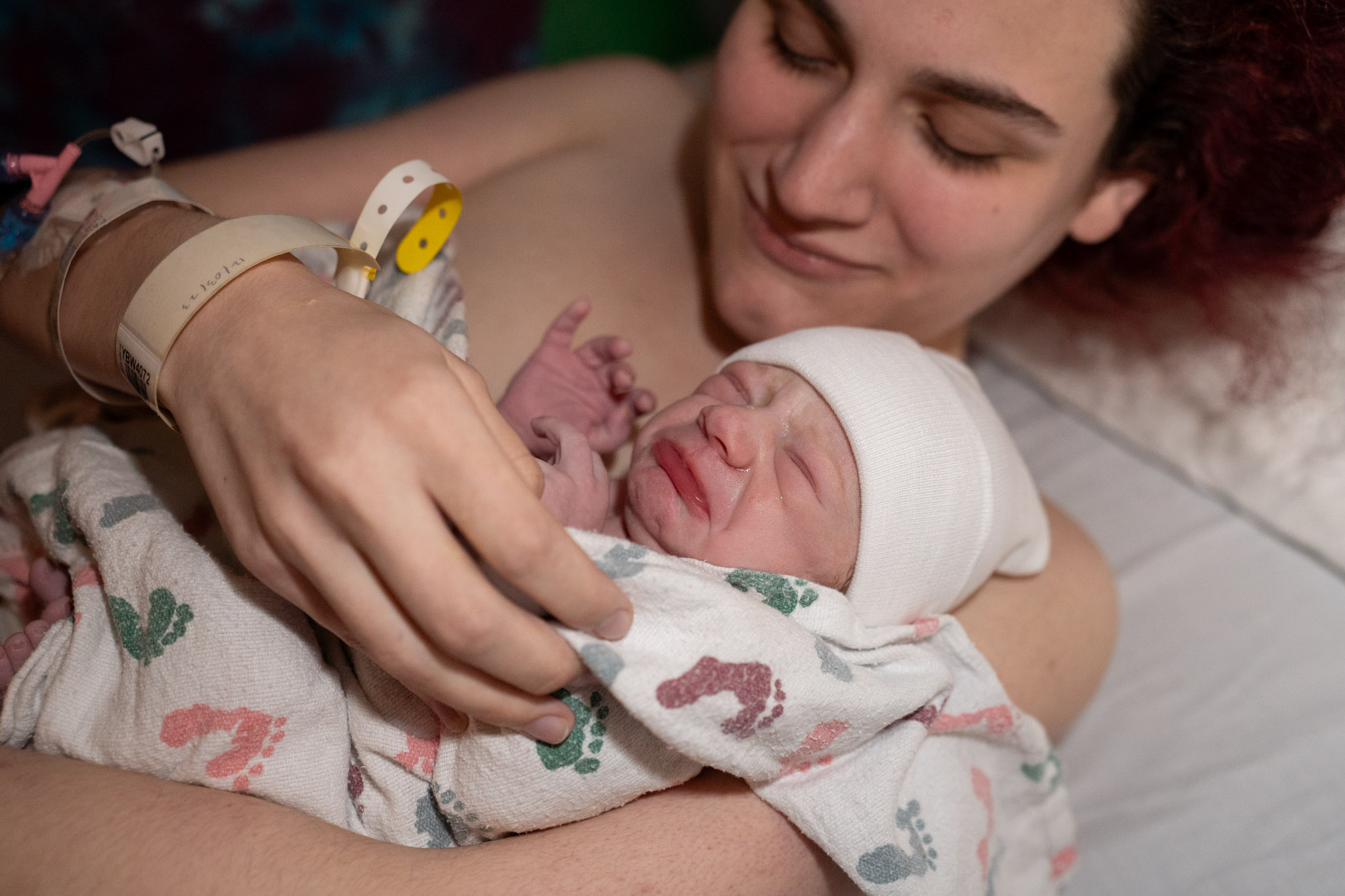 a smiling mother holds baby for the first time after giving birth while the baby is scowling