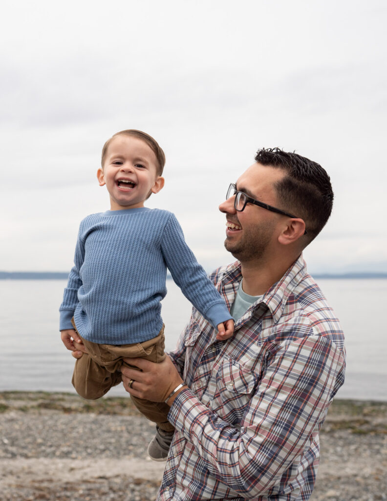 A dad is holding his laughing toddler at Carkeek Park 