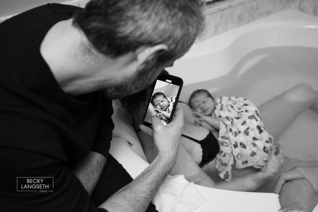 A dad takes a photo of his new baby in the arms of his wife who just gave birth and is still holding the baby in the birth tub at the Puget Sound Birth Center.