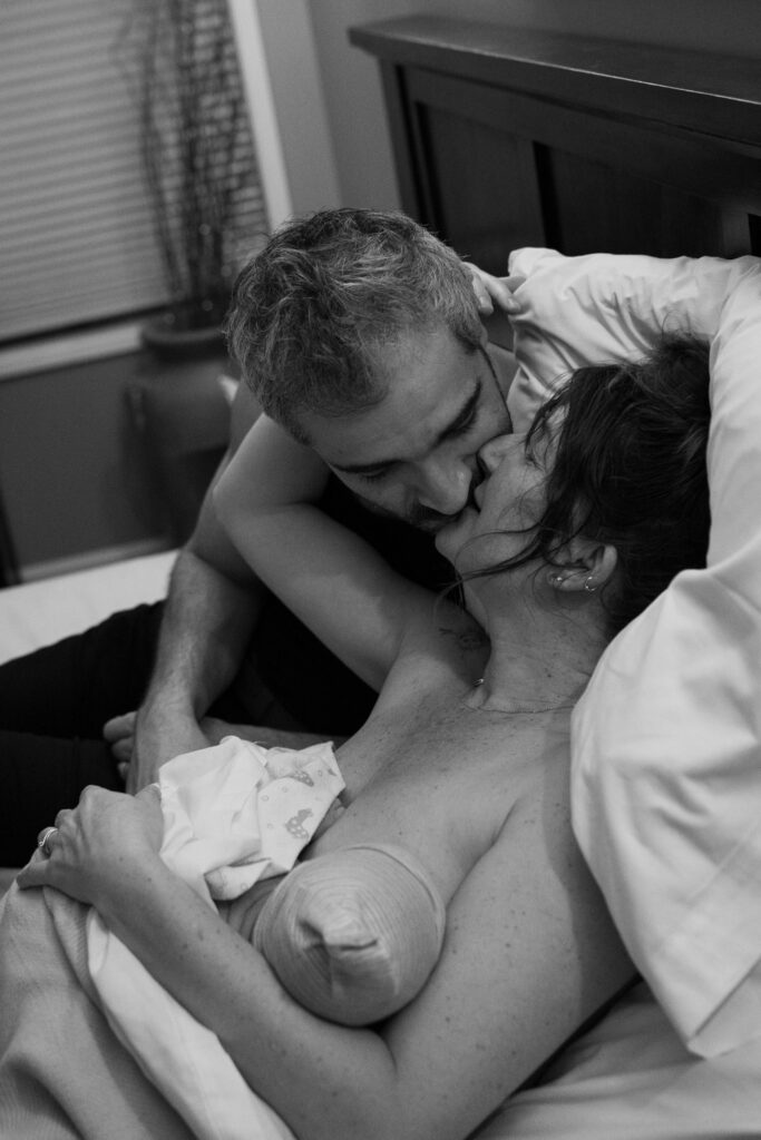 Mom and dad kiss in celebration of just giving birth, as mom holds baby.