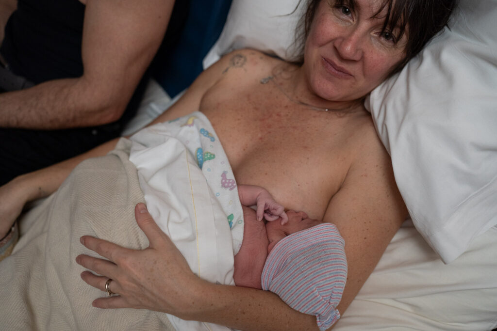 newly born baby breastfeeding as her mother looks at the camera in joy.