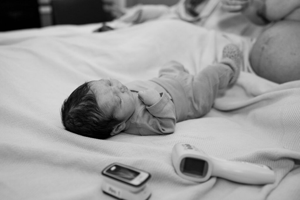 baby is dressed in newborn clothes and lying on the bed at the birth center after recently being born.