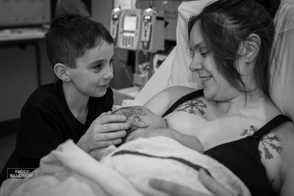 big brother looks at his mom who is holding his new baby sibling