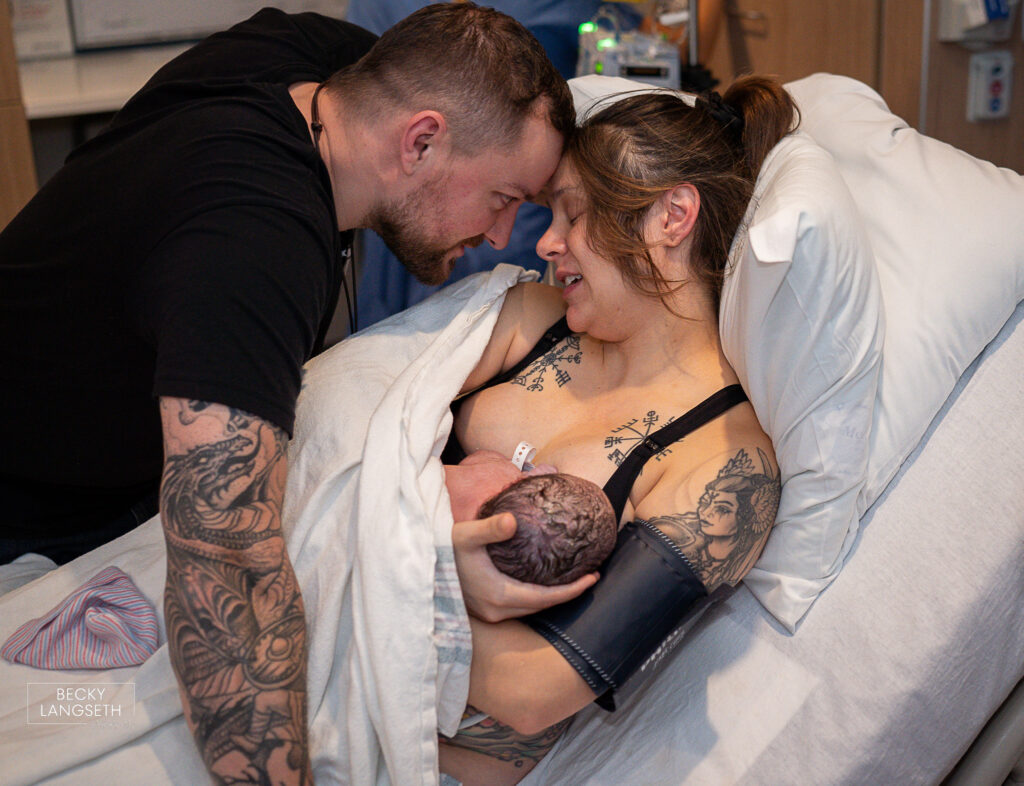 mom and dad have their heads together as they hold their newly born baby in the hospital after a transfer from a birth center