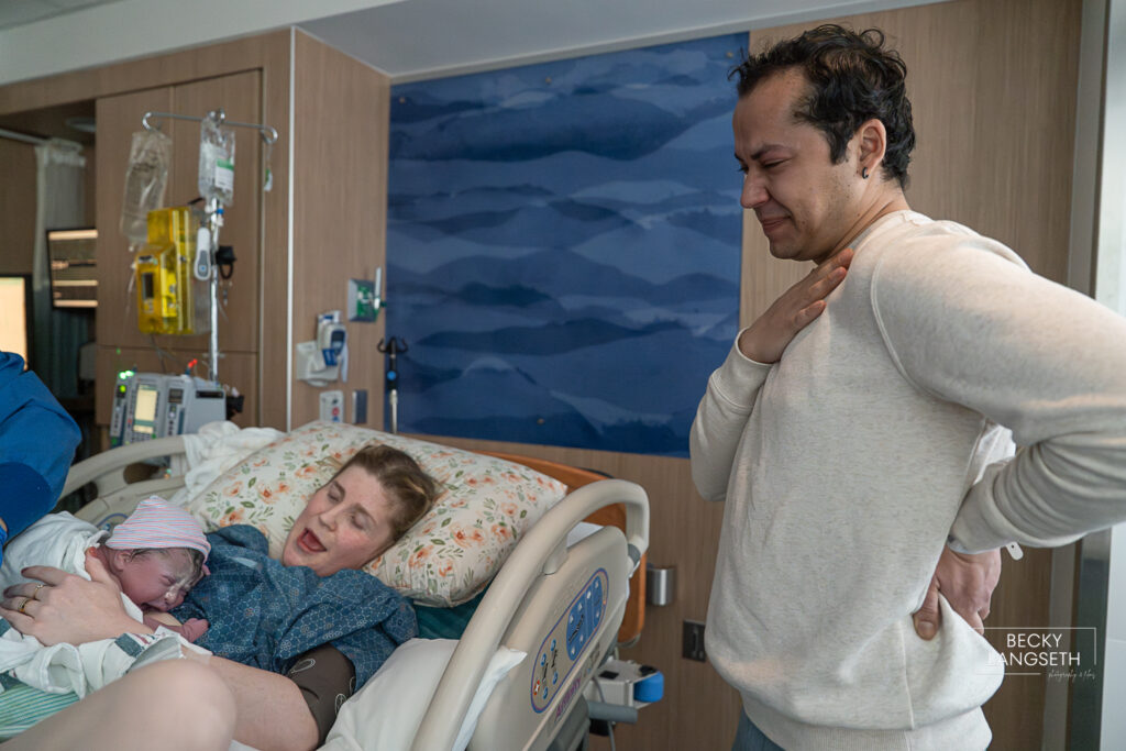 A father put his hand on his heart as he holds back tears after witnessing his wife give birth