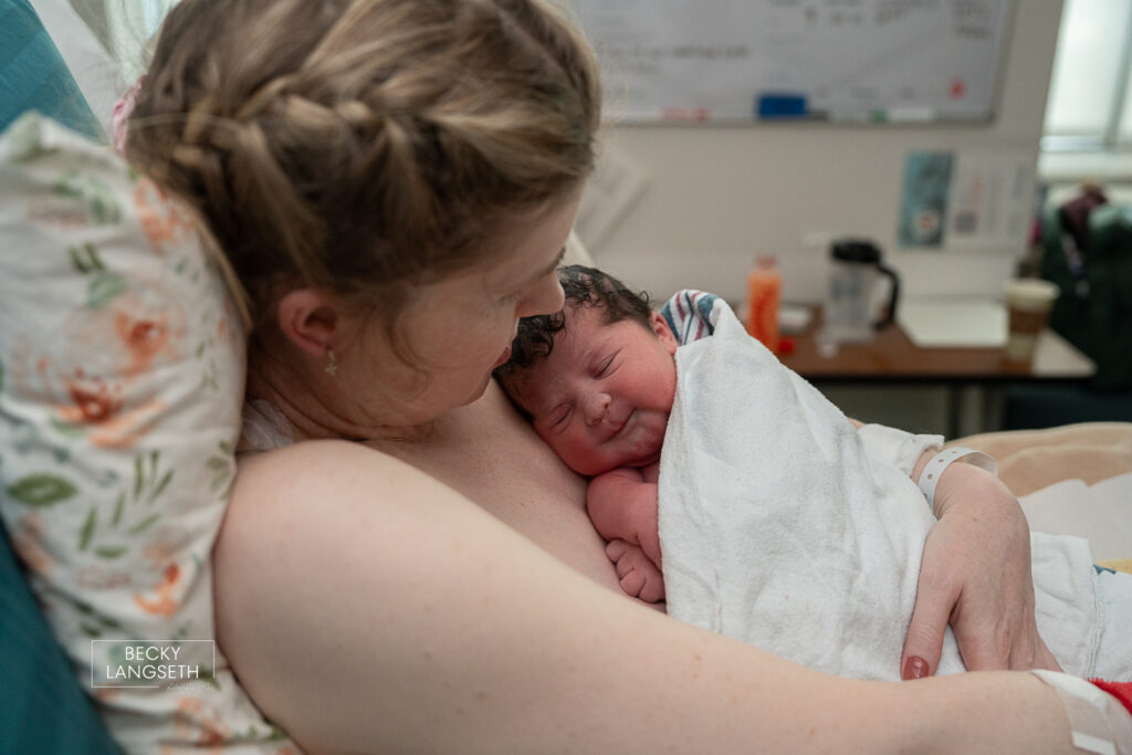 side view of a mother holding her baby for the first time after being born in a hospital bed.