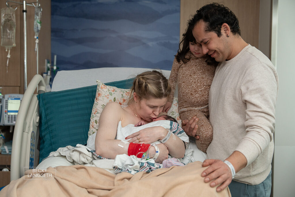a mother kisses her newly born baby as her husband holding her older daughter look at the new baby at Evergreen Hospital in Kirkland, WA