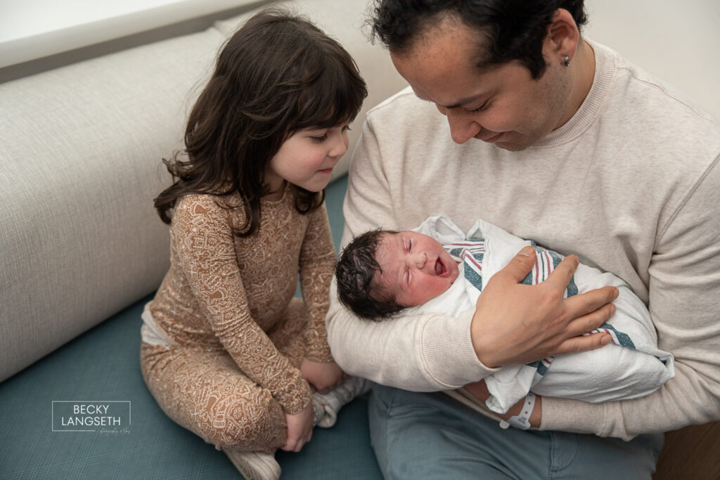 big sister looking at dad holding her newly born little sister at EvergreenHealth Medical Center