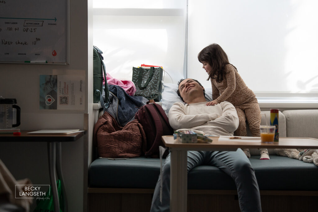 father smiles at his firstborn daughter as they wait for the new baby to be born