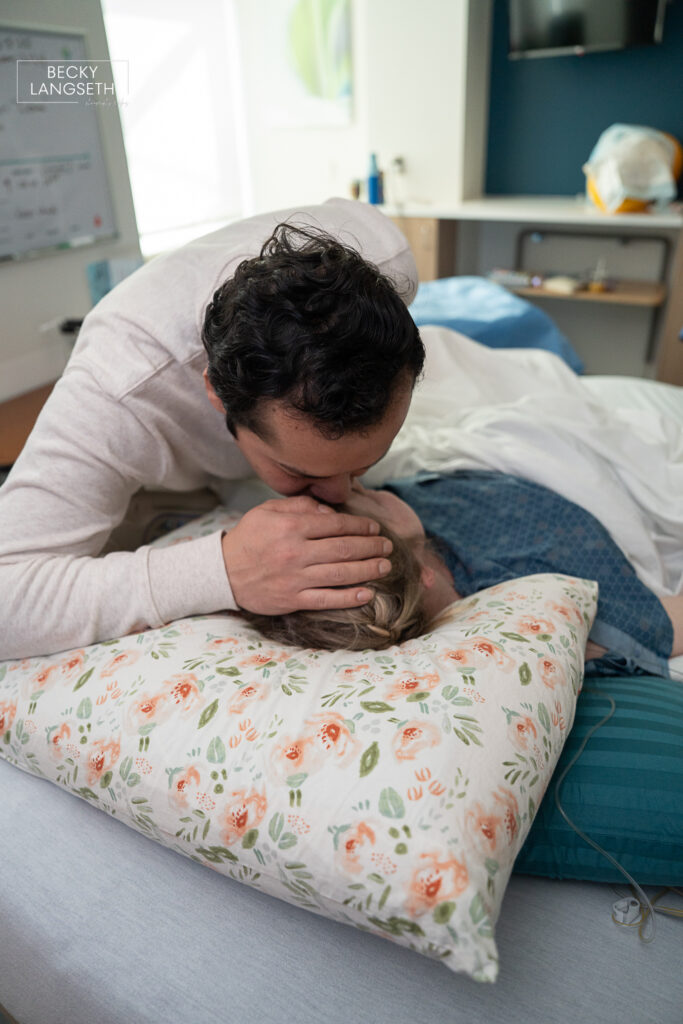 husband kisses his wife on the forehead right before she is about to give birth