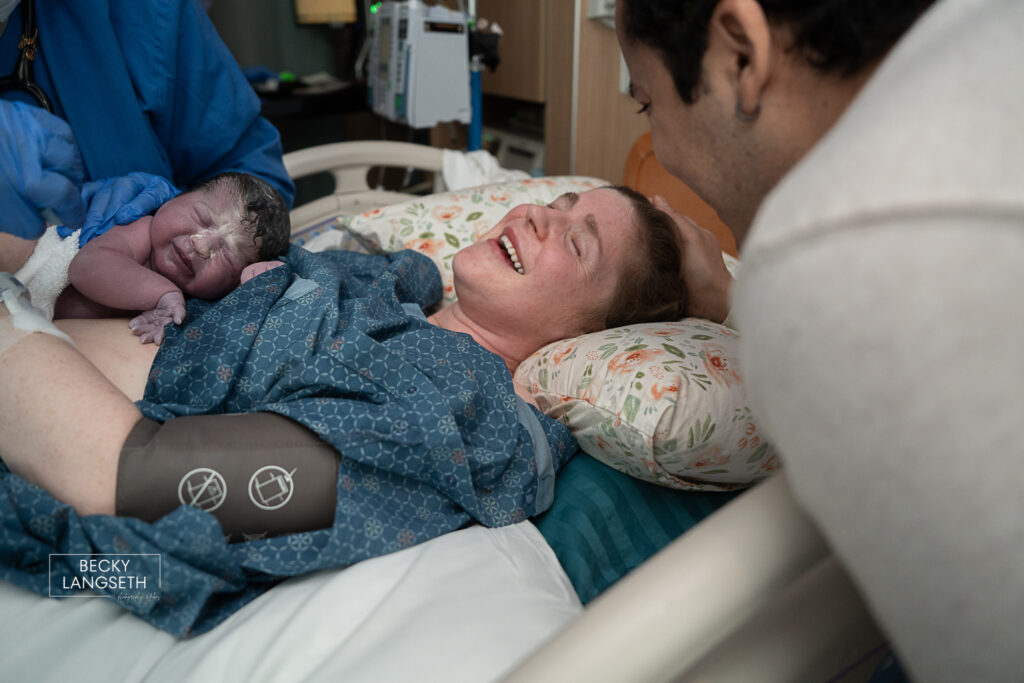 A mother closes her eyes and smiles with relief as she holds her baby after recently giving birth