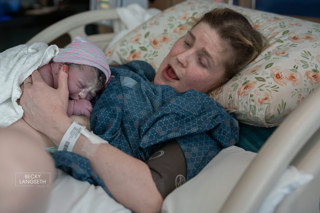 A mother looks at her newly born baby on her chest in a hospital bed at Evergreen Hospital