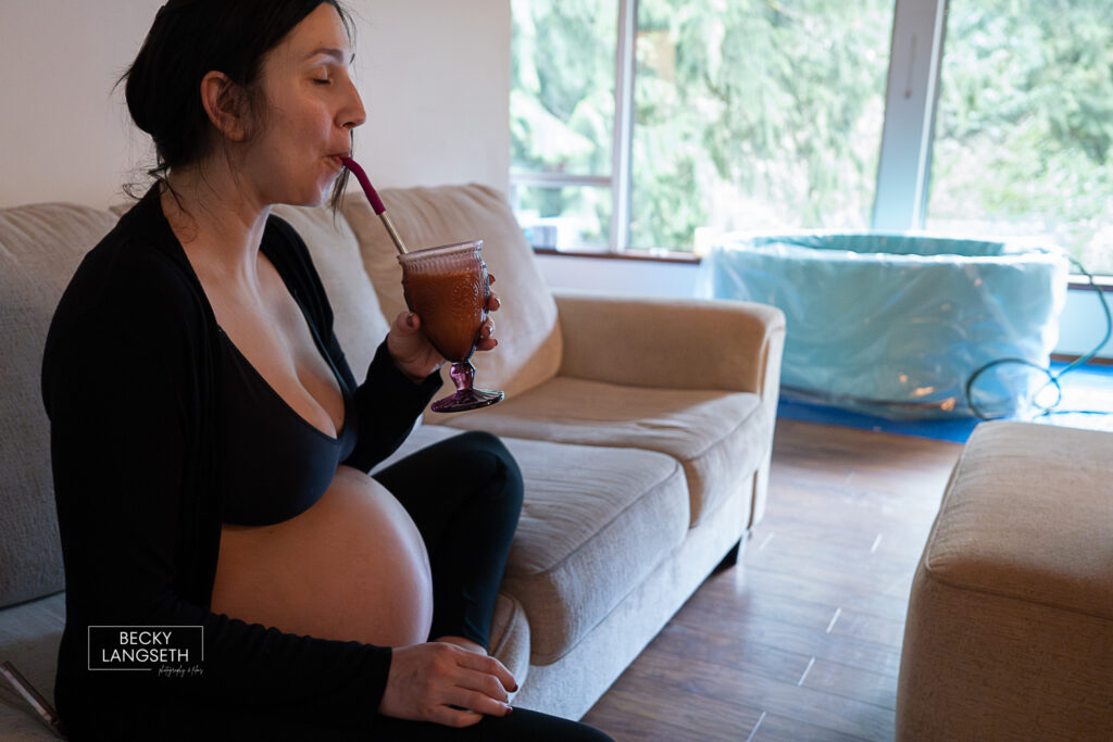 pregnant person sipping a smoothie in her home with a birth pool in the background