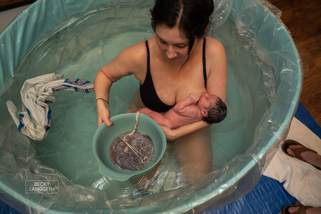 mom in a birth pool holding her new baby and the bowl of her placenta