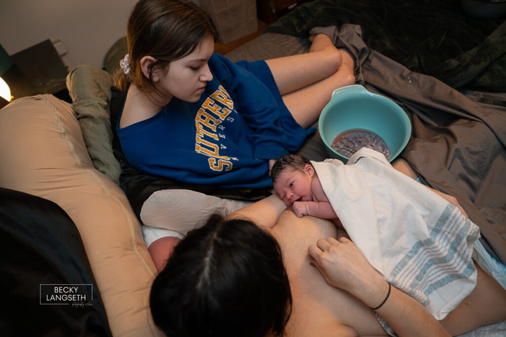 in bed at home with new baby and big sister after giving birth