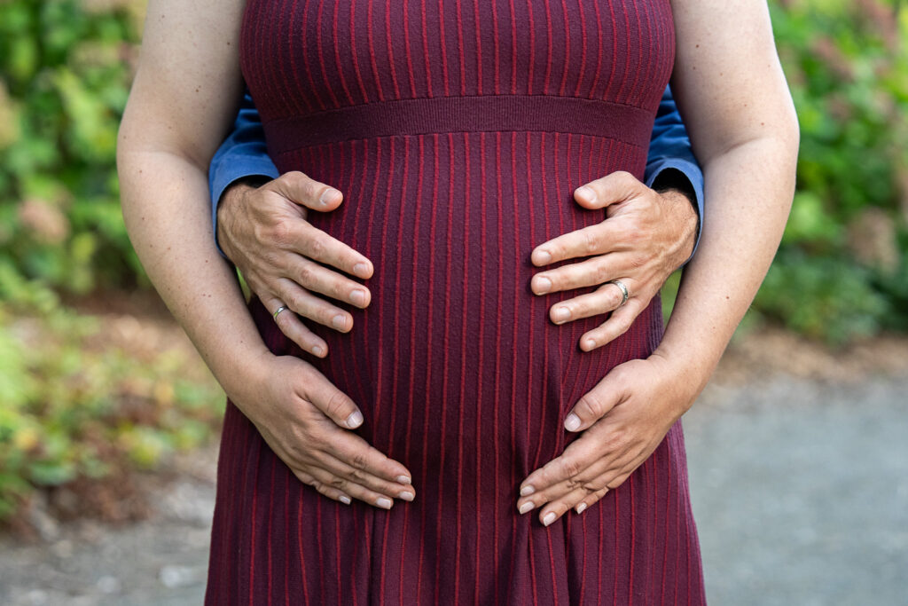 close up of a pregnant belly with the pregnant person's hands and partners hands surrounding it